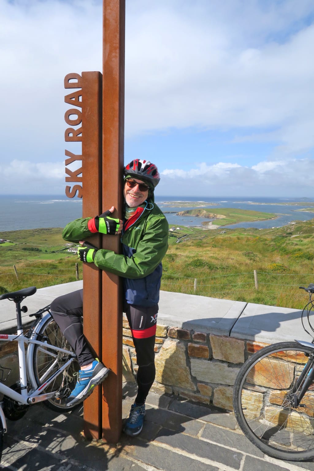Ciclista in viaggio con "Girolibero" accanto a un segnale del Wild Atlantic Way, Connemara, Irlanda, con vista sull'oceano.